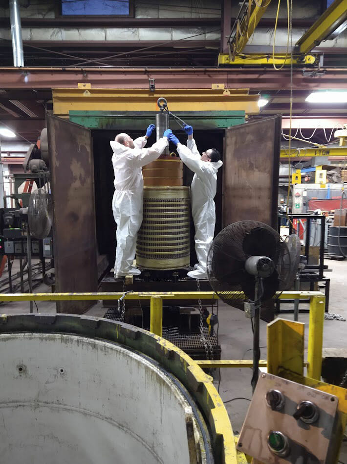 Two men in white uniforms securing a generator into a bake oven.